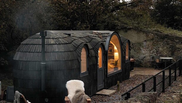 A cozy cabin with a fireplace, a chair, and a table outside. - Whole Coastal Estate · Sleeps 12 · Anglesey (Isle of Anglesey)