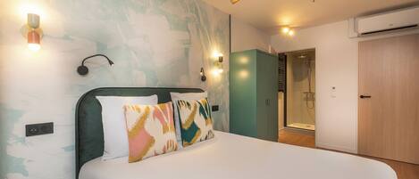A modern hotel room with a large bed, a shower area, and a wardrobe.