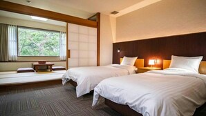 Ein Hotelzimmer mit zwei Betten, einem kleinen Tisch und einem Fenster mit Blick auf Grünflächen.