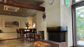 Eine Lobby mit Steinboden, Kamin, einer Uhr und einem Essbereich mit Stühlen und einem Tisch.