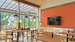 Ein Restaurant mit Holztischen und -stühlen, großen Fenstern und einem Fernseher an der Wand.