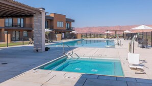 A rooftop pool area with clear blue water, lounge chairs, and umbrellas, surrounded by modern buildings and mountains in the background. - Next to Pool, Sleek & Modern 3BR w/Fireplace (St. George)