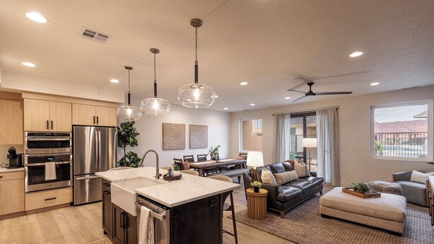 A modern kitchen with stainless steel appliances, a central island, pendant lighting, and a dining area with a sofa and table. - Next to Pool, Sleek & Modern 3BR w/Fireplace (St. George)