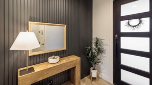 A modern entryway with a dark wood panel wall, a wooden console table with a mirror, a lamp, and a potted plant. - Next to Pool, Sleek & Modern 3BR w/Fireplace (St. George)