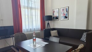 A modern living room with a dark sofa, a dining table with chairs, a floor lamp, and a TV. - Bright Studio Apartment in Konstanz (Konstanz)