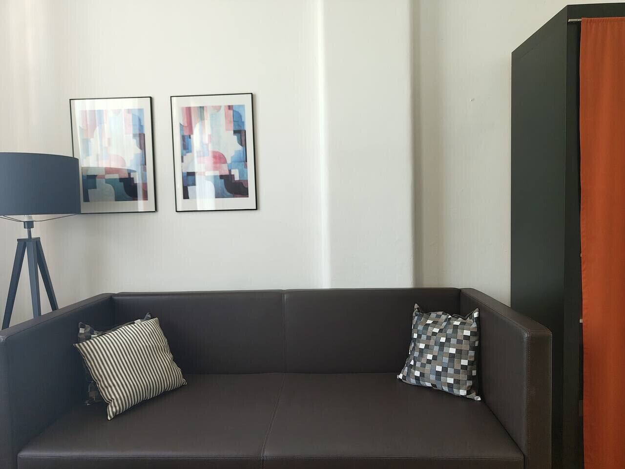 Un canapé brun foncé agrémenté de deux coussins, un lampadaire et deux tableaux abstraits accrochés au mur.
