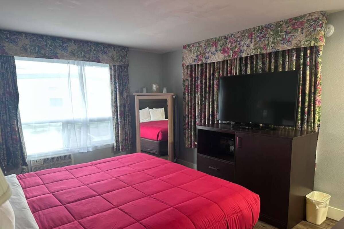 A hotel room with a large bed, a television, a wardrobe, and a window with curtains.