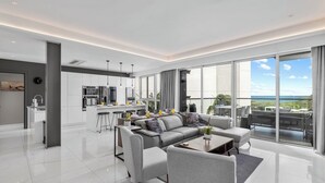 Ein modernes Wohnzimmer mit grauem Sofa, einem Couchtisch und einem großen Fenster mit Blick auf den Ozean.