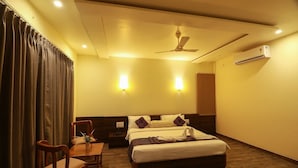 A hotel room with a bed, a desk with chairs, a ceiling fan, and wall-mounted lights. - Hotel The Cult (Hubli)