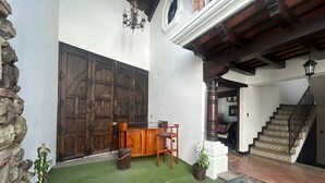Un patio con un banco de madera, una mesita y plantas en macetas. Se ve una escalera que sube a un nivel superior.