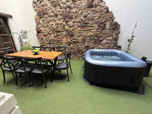 A patio with a stone wall, a wooden table with chairs, and a hot tub. - Beautiful house in the historic center of Antigua Guatemala with a Jacuzzi (Antigua Guatemala)