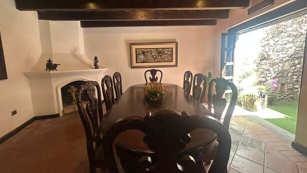 Une salle à manger avec une grande table en bois, des chaises décorées, une cheminée et un tableau encadré au mur.
