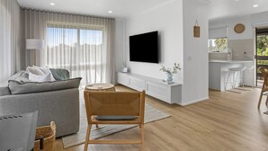 Uma sala de estar moderna com sofá, televisão e área de jantar, com cozinha ao fundo.