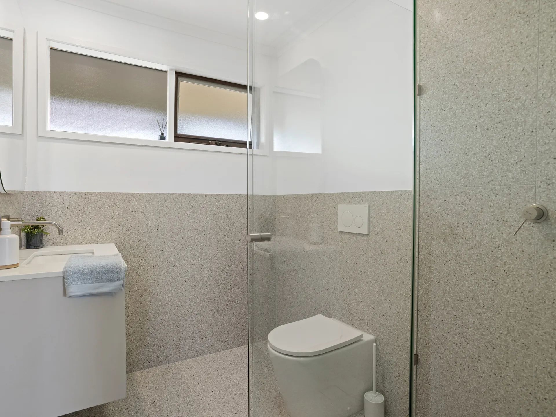 Une salle de bain moderne avec une douche à parois de verre, des toilettes blanches et un lavabo avec une serviette.