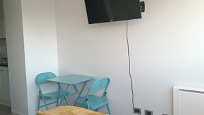 Ett sovrum med en säng, en tv som är monterad på väggen och ett litet bord med stolar.