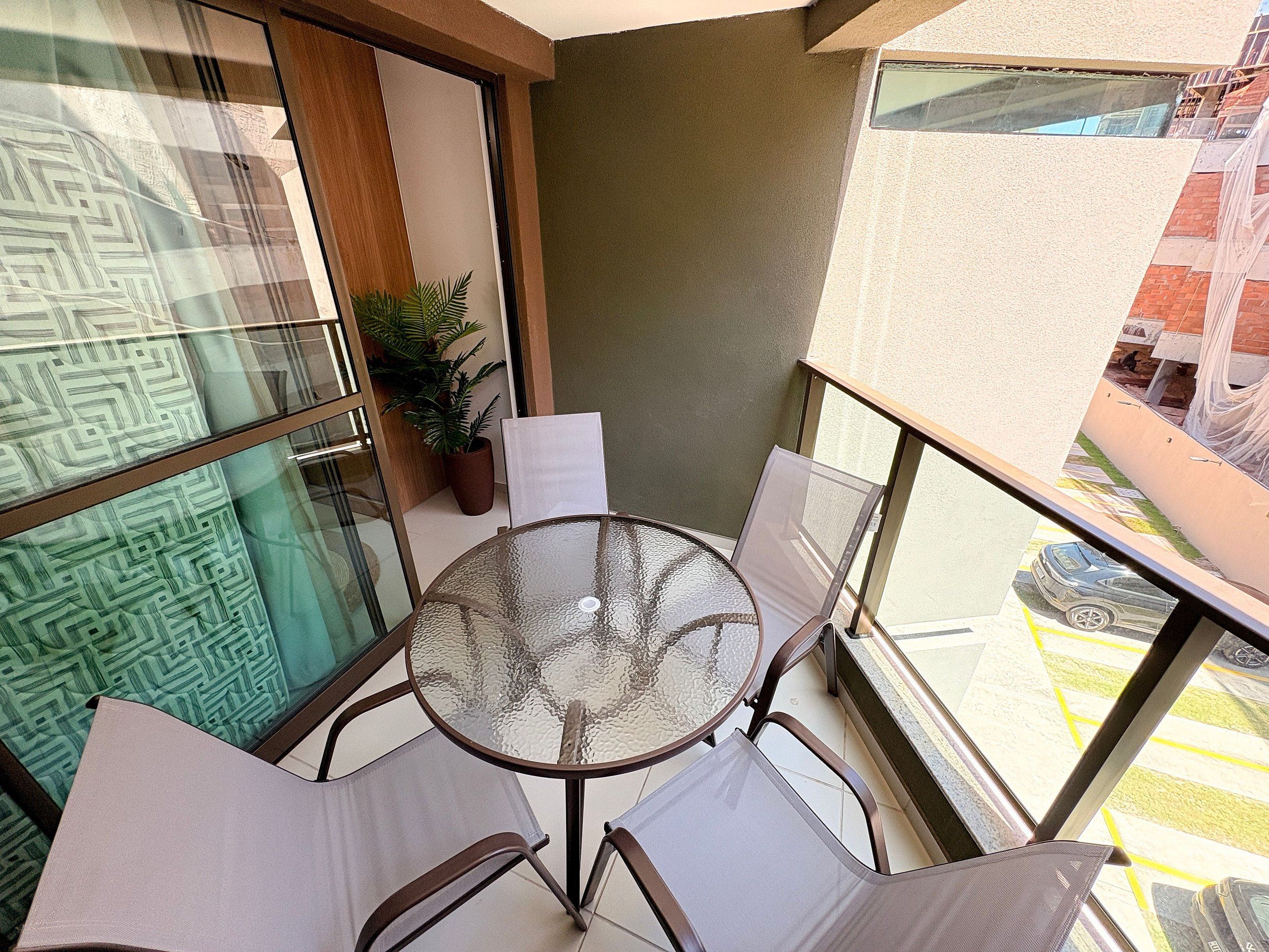 A balcony with a glass table and chairs, a potted plant, and a view of a parking area.