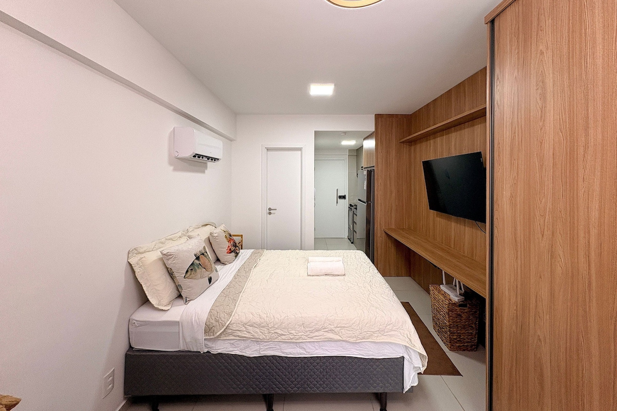 A bedroom with a bed, a television mounted on a wooden wall, and a white air conditioning unit on the wall.
