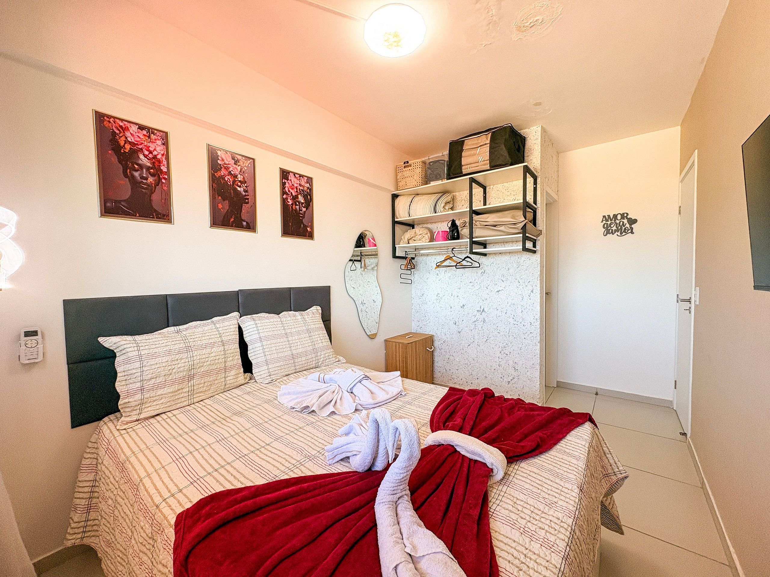 A bedroom with a bed, a shelf with folded blankets, and three framed pictures on the wall.