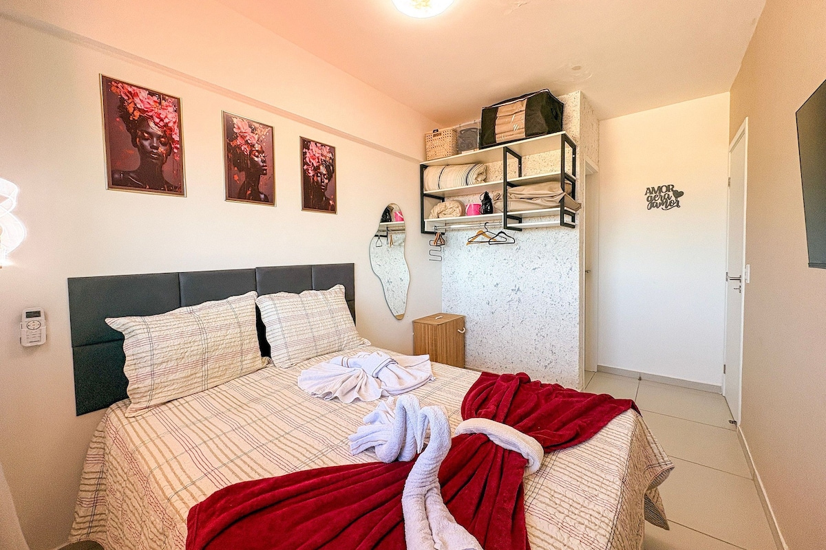 A bedroom with a bed, a shelf with folded blankets, and three framed pictures on the wall.