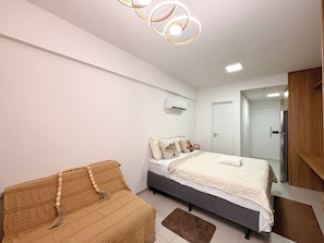 A bedroom with a bed, a sofa, a ceiling light fixture, and a door. - Açores Praia de Tamandaré - À Beira-Mar (Tamandaré)