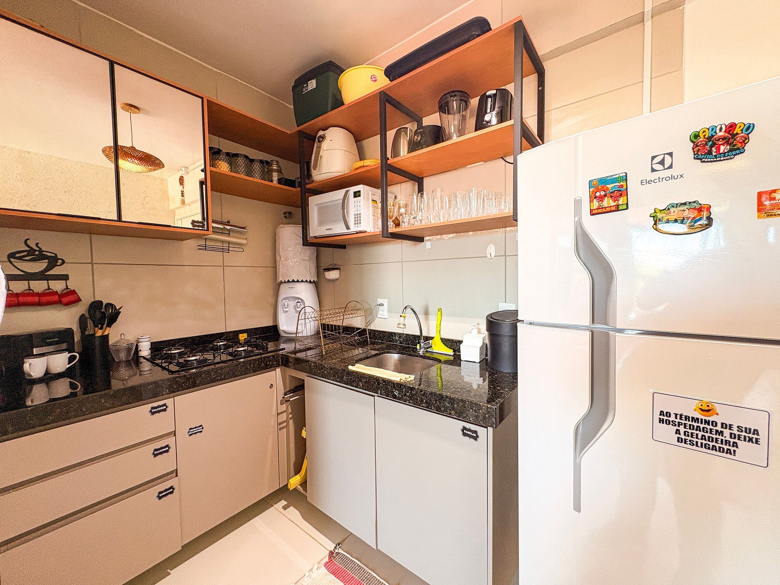 A kitchen with a refrigerator, microwave, and stove. There are cabinets, a sink, and a shelf with kitchen items.