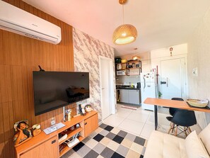 A living room with a flat-screen TV, wooden entertainment unit, checkered floor, and a dining area with a table and chairs. - Açores Praia de Tamandaré - À Beira-Mar (Tamandaré)