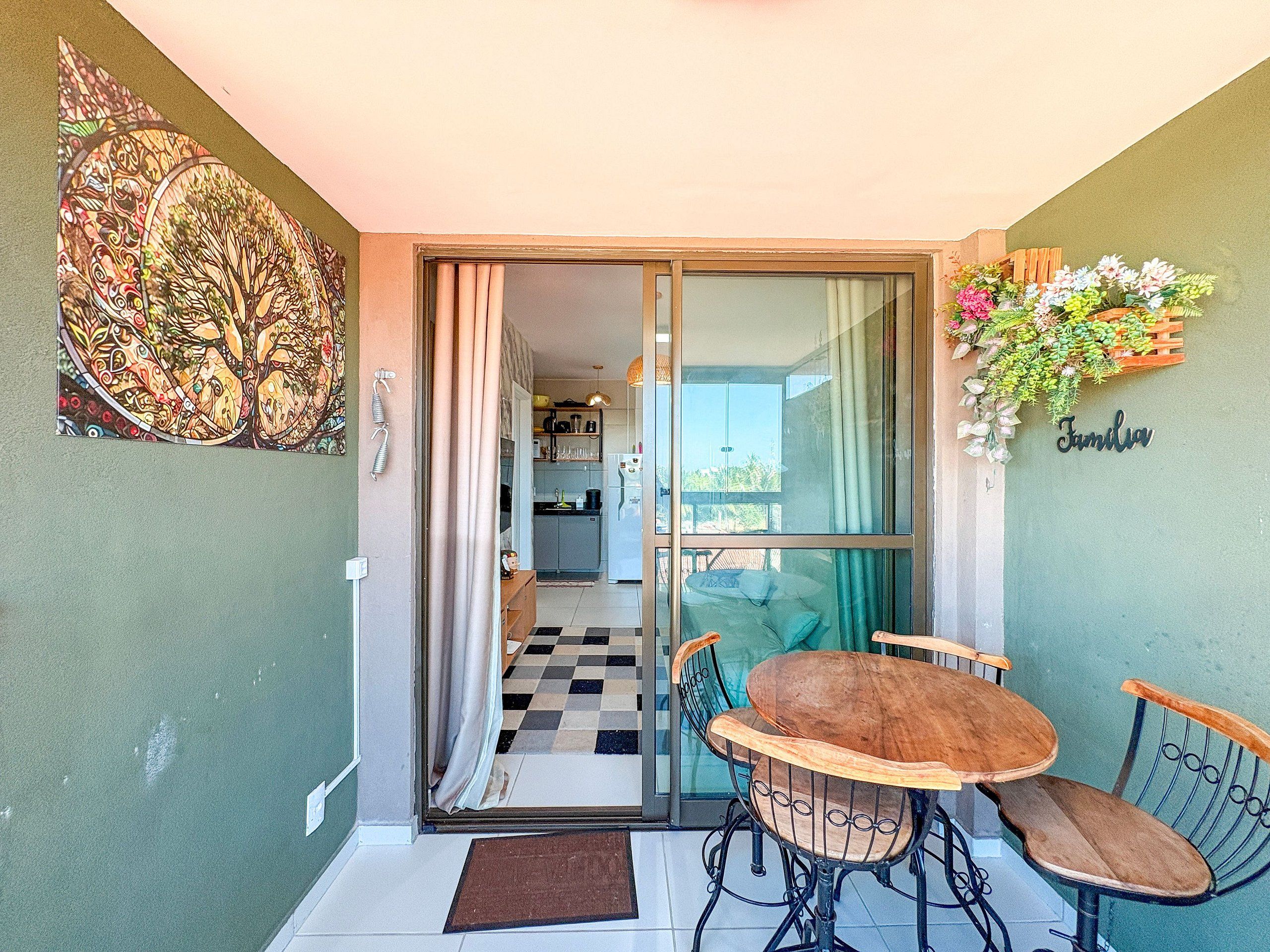 A dining area with a table and chairs, a kitchen in the background, and a sliding glass door leading to a balcony with a flower arrangement.
