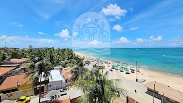 Uma área costeira com praia, palmeiras e céu claro.