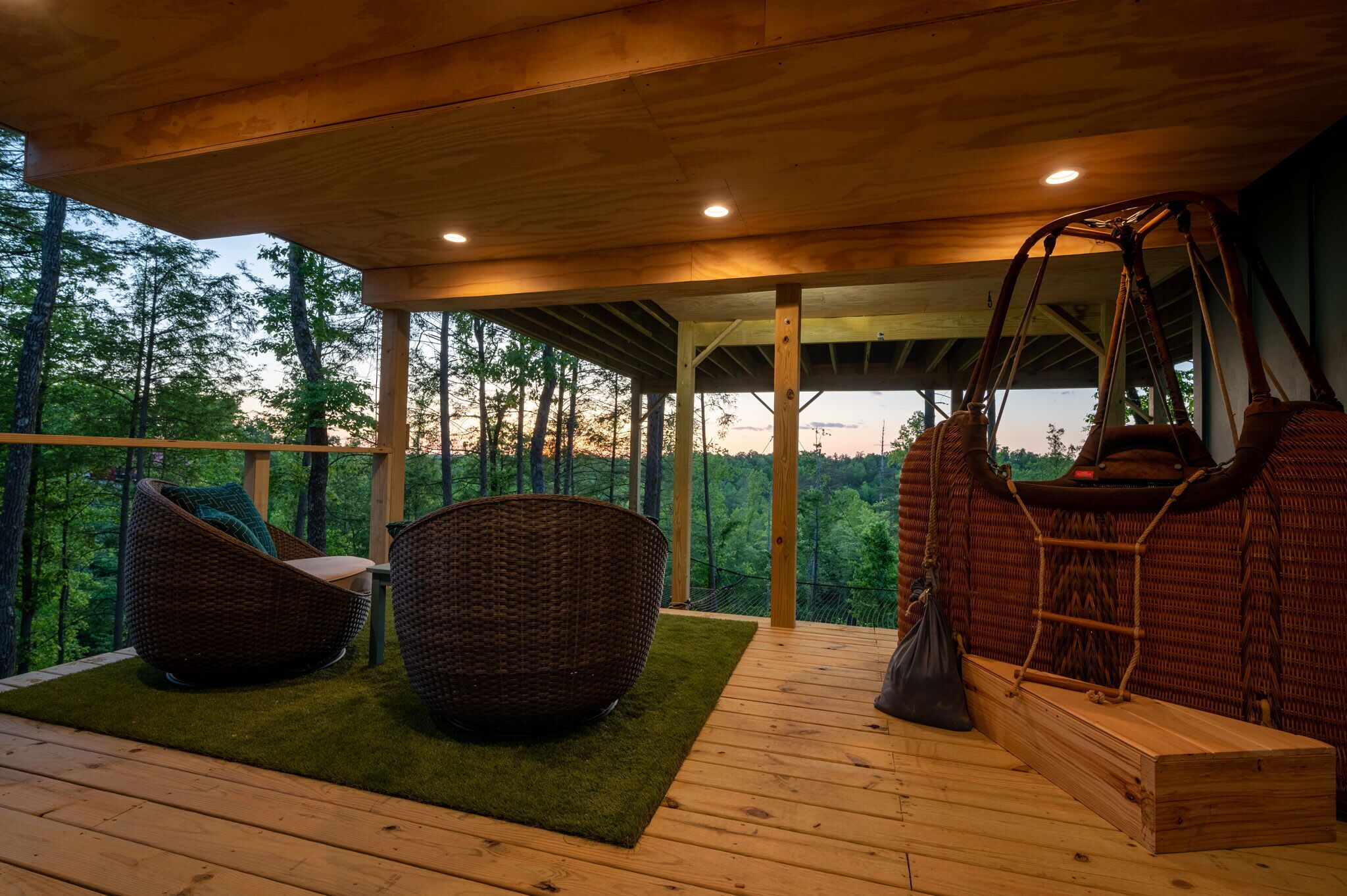 A wooden deck with wicker furniture, a swing, and a view of a forest.