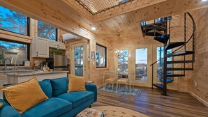 Ein gemütliches Blockhaus-Interieur mit einem blauen Sofa, Holzböden, einer Wendeltreppe und großen Fenstern.