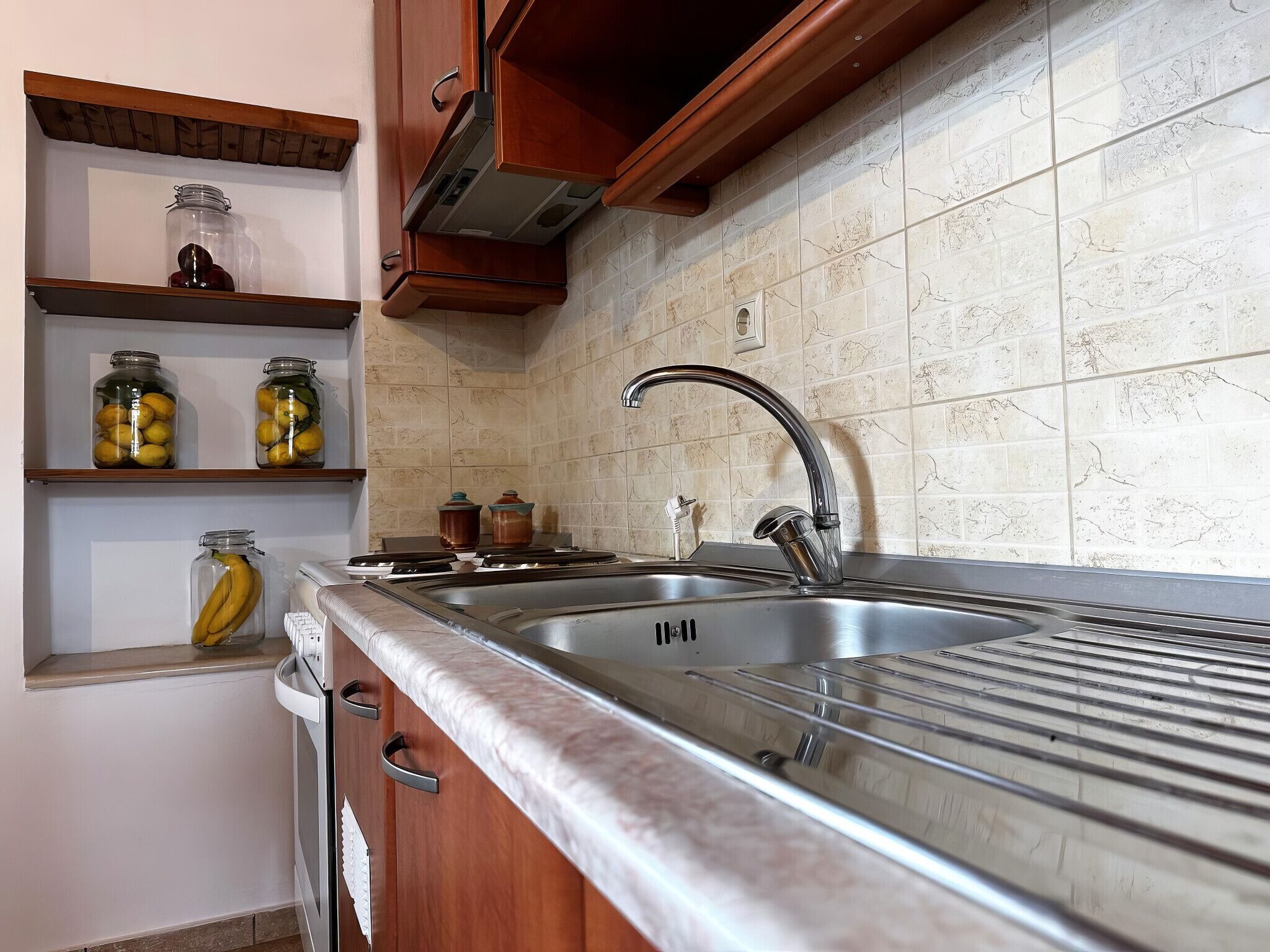 A kitchen with a stainless steel sink, wooden cabinets, and a tiled backsplash.