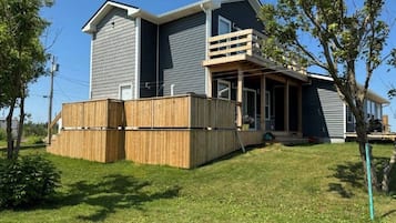 Une maison à deux étages avec un balcon, une terrasse en bois et une cour gazonnée.