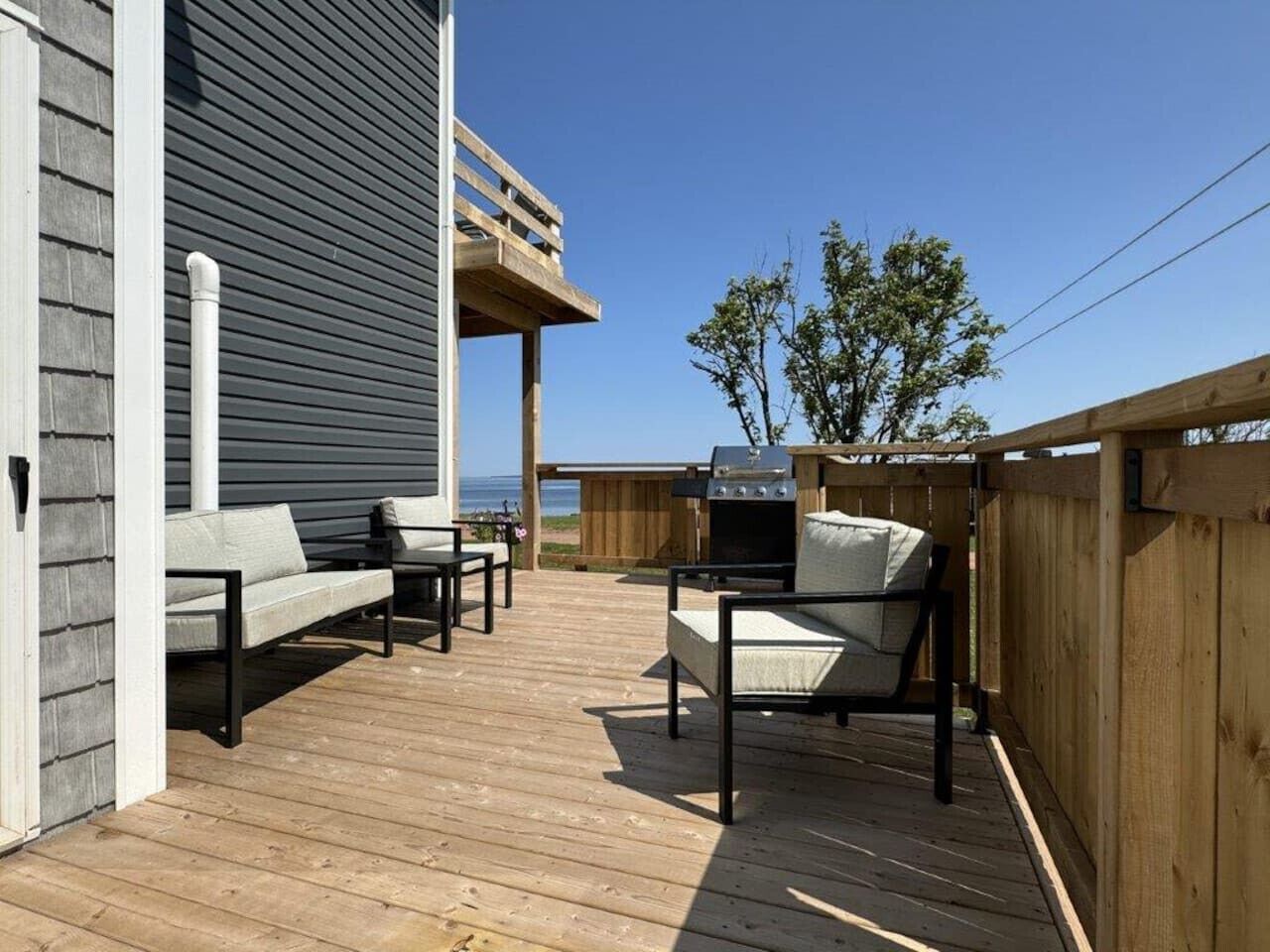Une terrasse extérieure avec un plancher en bois, deux canapés, un barbecue et une clôture en bois.