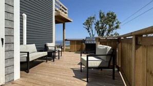 Eine Terrasse im Freien mit Holzboden, zwei Sofas, einem Grill und einem Holzzaun.