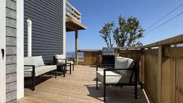 Une terrasse extérieure avec un plancher en bois, deux canapés, un barbecue et une clôture en bois.