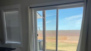Ein modernes Wohnzimmer mit einer großen Schiebeglasdoor, die auf eine Terrasse führt. Es gibt ein Sofa und einen kleinen Tisch mit einem Buch darauf.
