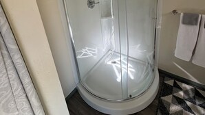 Una ducha con cerramiento de vidrio, suelo de baldosas blancas y un tapete estampado.