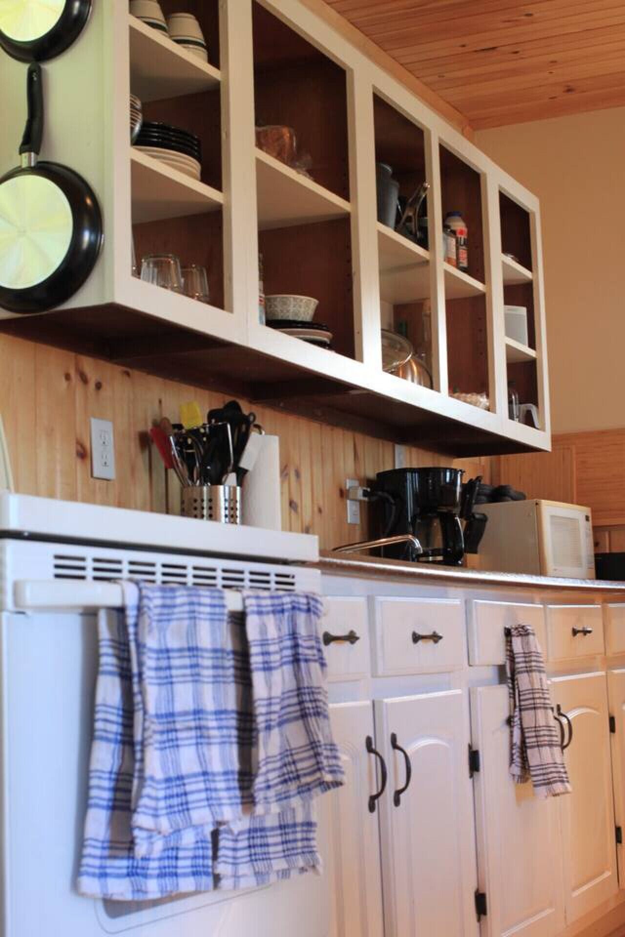 A kitchen with white cabinets, a microwave, and a coffee maker. There are two plaid kitchen towels hanging on the oven door.