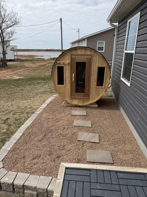 A wooden structure with a door and windows, placed on gravel with stepping stones leading to it, next to a house.