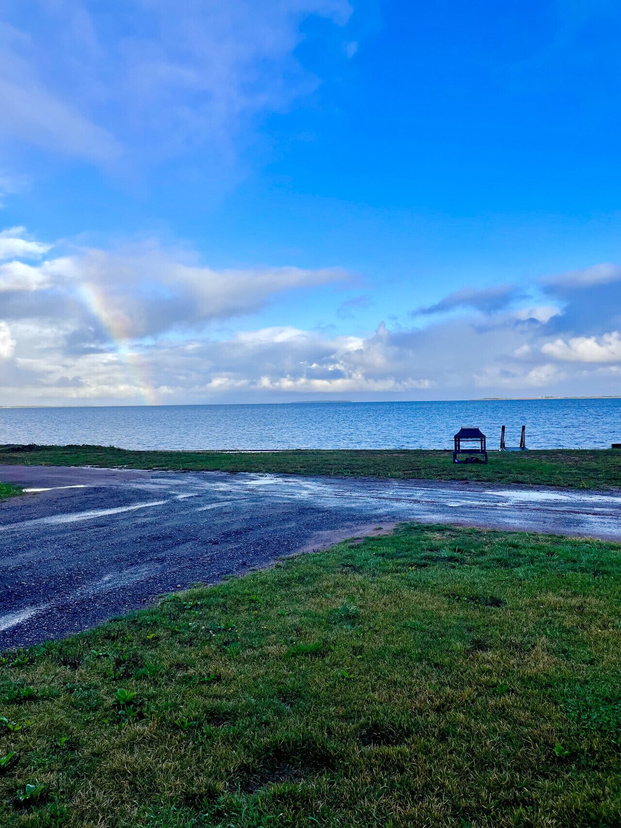 Une zone herbeuse avec un banc et une petite construction située près du bord de l’eau.