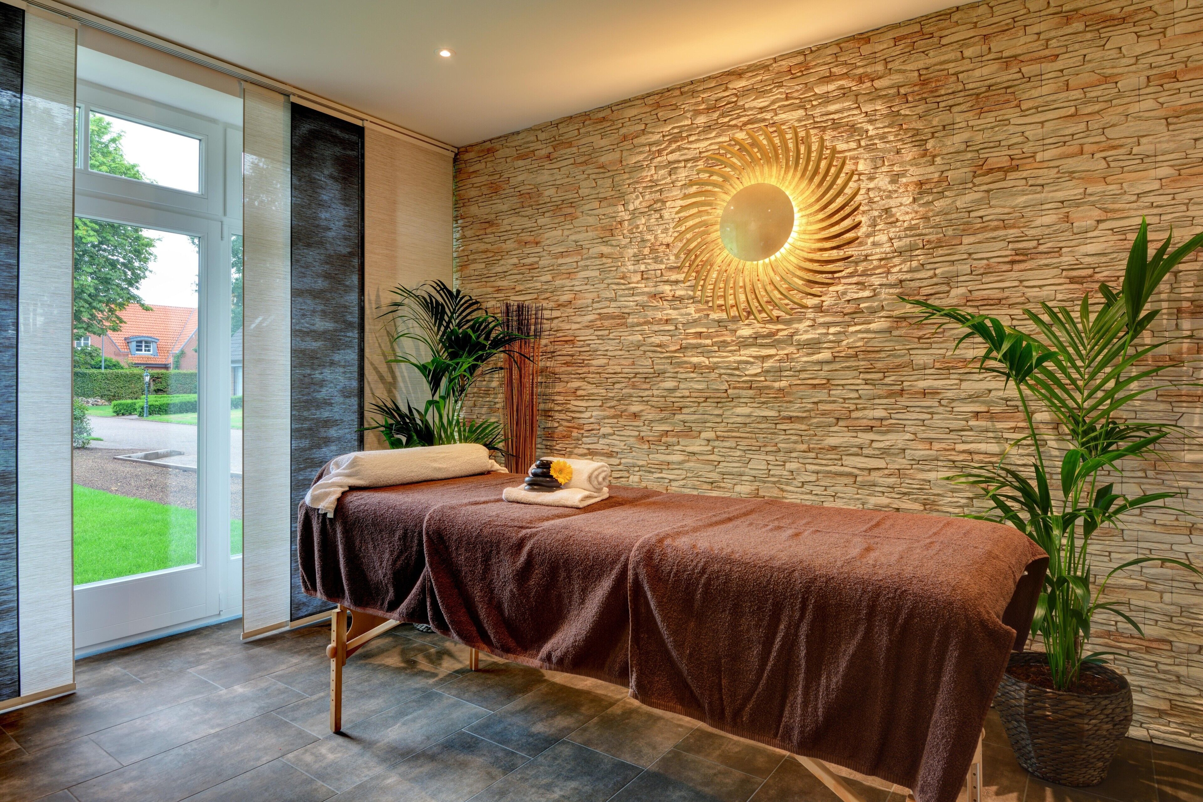 Un cuarto de spa con una camilla de masaje, una pared de piedra, un espejo grande y una planta en maceta.