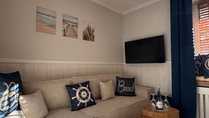 Una sala de estar con un sofá, televisión, una mesa de centro de madera y una alfombra estampada.