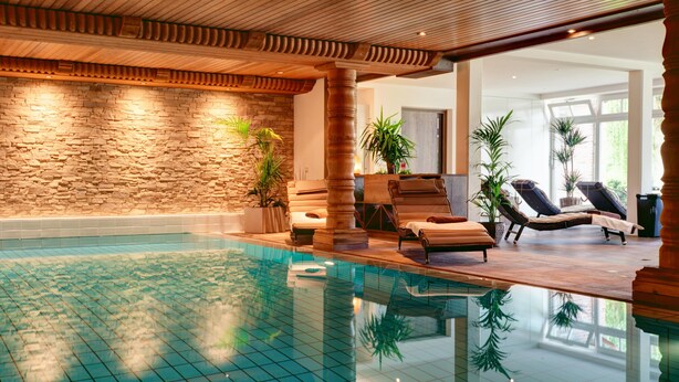 An indoor swimming pool with tiled flooring, wooden beams, stone walls, and lounge chairs. - Apartment in 'Haus Anni' with Terrace and Wi-Fi (Bad Zwischenahn)