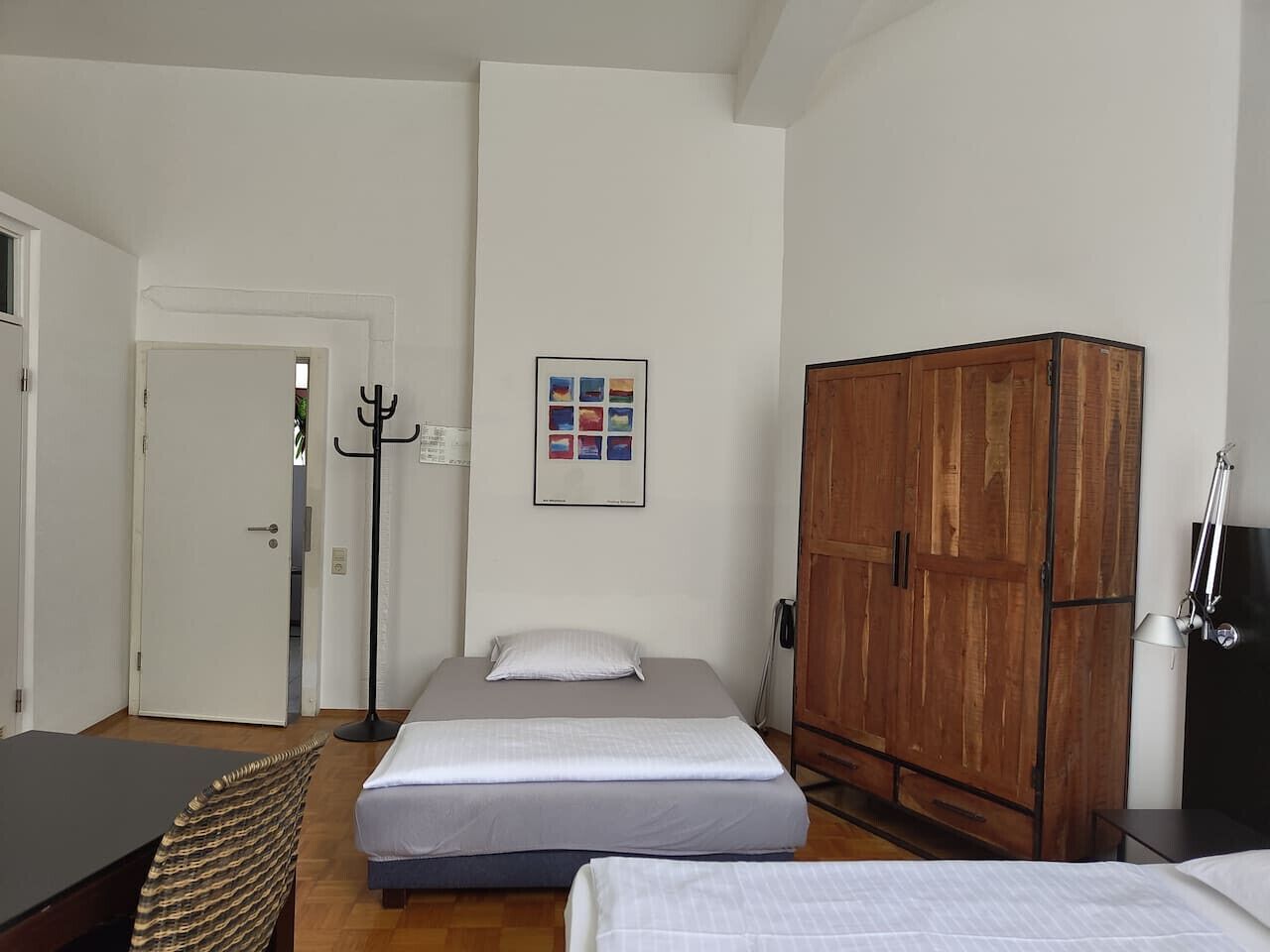 A bedroom with a bed, a wardrobe, a coat rack, and a framed picture on the wall.