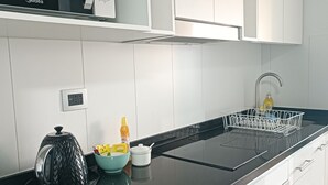 A modern kitchen with white cabinets, a black countertop, a microwave, a kettle, and a sink. - Kasa y Familia 724 (Valdivia)