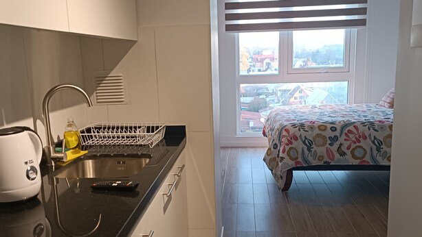 A compact kitchen with modern appliances, a dining area, and a bedroom with a window view. - Kasa y Familia 724 (Valdivia)