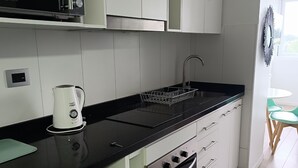 Une cuisine moderne avec des armoires blanches, un plan de travail noir, un four encastré et un four à micro-ondes.