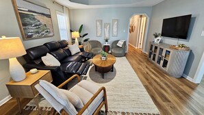Ein modernes Wohnzimmer mit einem schwarzen Ledersofa, einem Holztisch und einem grauen Sessel.