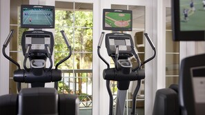 Two exercise bikes with screens displaying sports games, positioned in a room with large windows and a view of greenery outside. - 2-bedroom resort in superb Hilton Head Island; site of the PGA's RBC Classic. (Hilton Head Island)