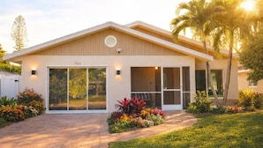 A modern two-story house with a number '764' on the front, large glass doors, and a well-maintained garden with various plants and flowers. - Modern Coastal Villa • Private Fenced Yard • Minutes to the Beach (Naples)